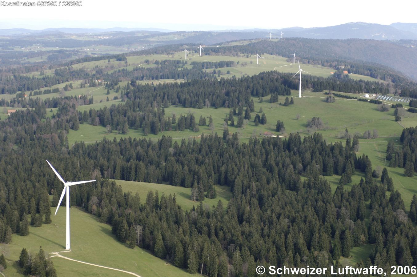 Mont Crosin: Centrale éolienne (Position: 2'567'886.23, 1'225'155.28) - Erste drei Turbinen um 1996, Erweiterung 1998, 2001 und 2004. Aufrüstung 2013 und 2016 mit totaler Leistung von 37,2 MW. der insgesamt 16 Turbinen. 2017 erreichte das Windkraftwerk eine Jahresproduktion von 74 Mio KWh. - Die Gondel der Turbinen liegt auf 95 Meter über dem Boden, ein Rotorblatt ist 45 Meter lang, Drehleistung ab 7 km/h bis 14 km/h Wind, macht 9 bis 15 Umdrehungen / Minute. Der Windpark versorgt etwa 13'000 Haushalte mit Strom. - Am rechten oberen Bildrand: 'Centrale solaire du Mont Soleil'.